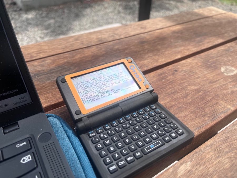 Orion PDA open on a wooden table next to a laptop